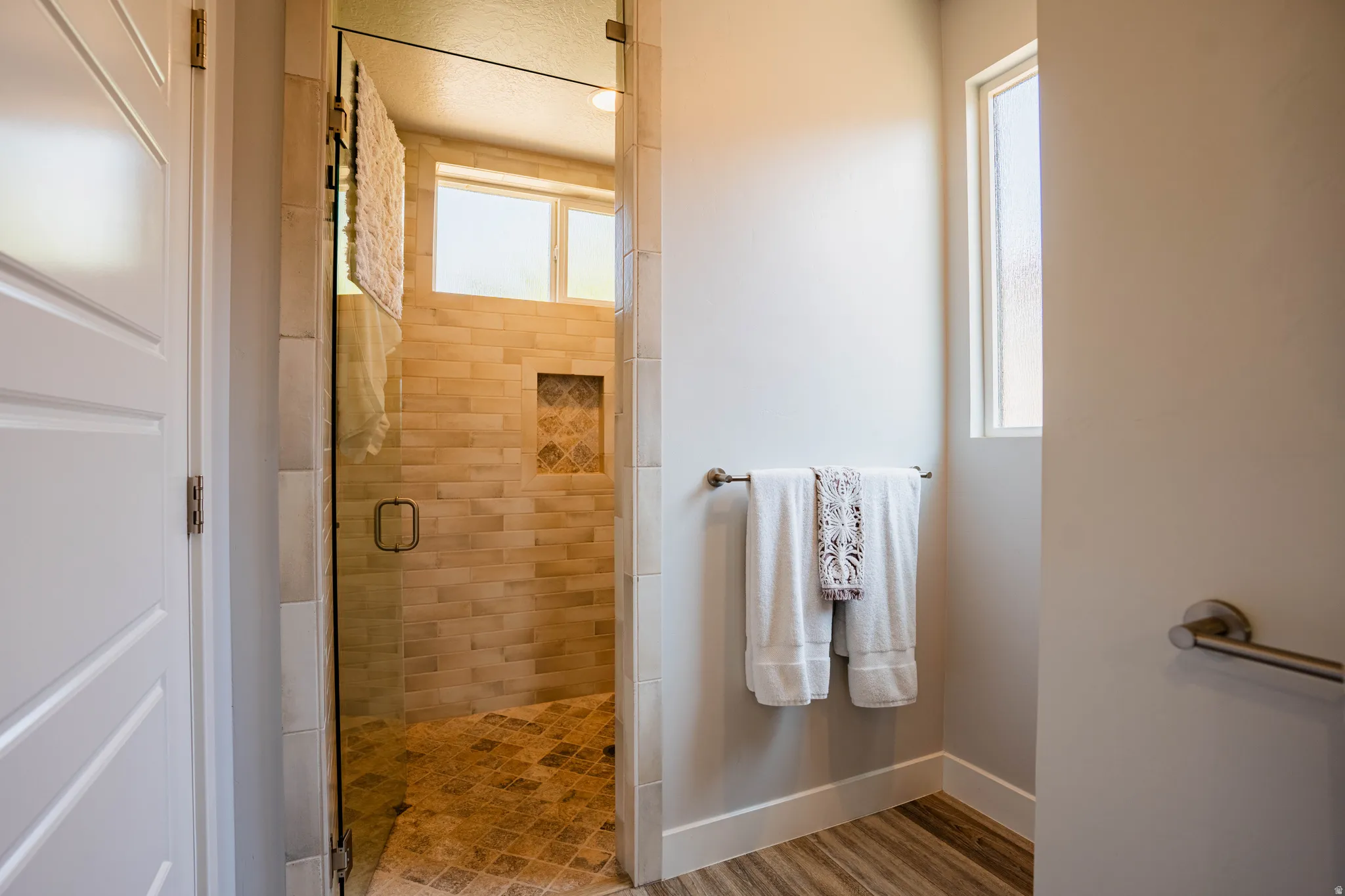 Glass-enclosed shower with subway tile walls, a decorative tile niche, and a patterned tile floor