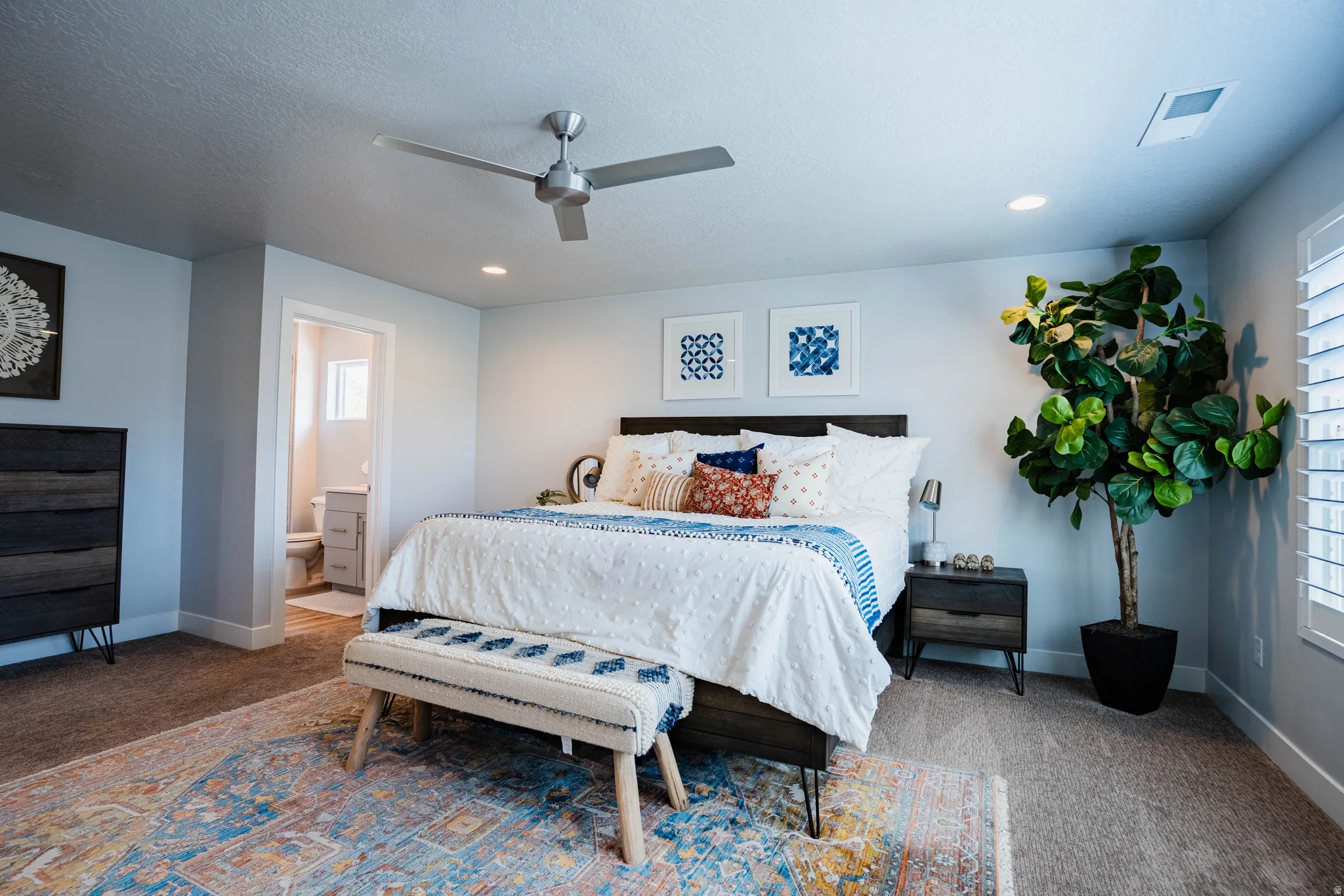 Recessed lighting, ceiling fan, carpet flooring, a built-in window shutter, and an open doorway to a bathroom with a window