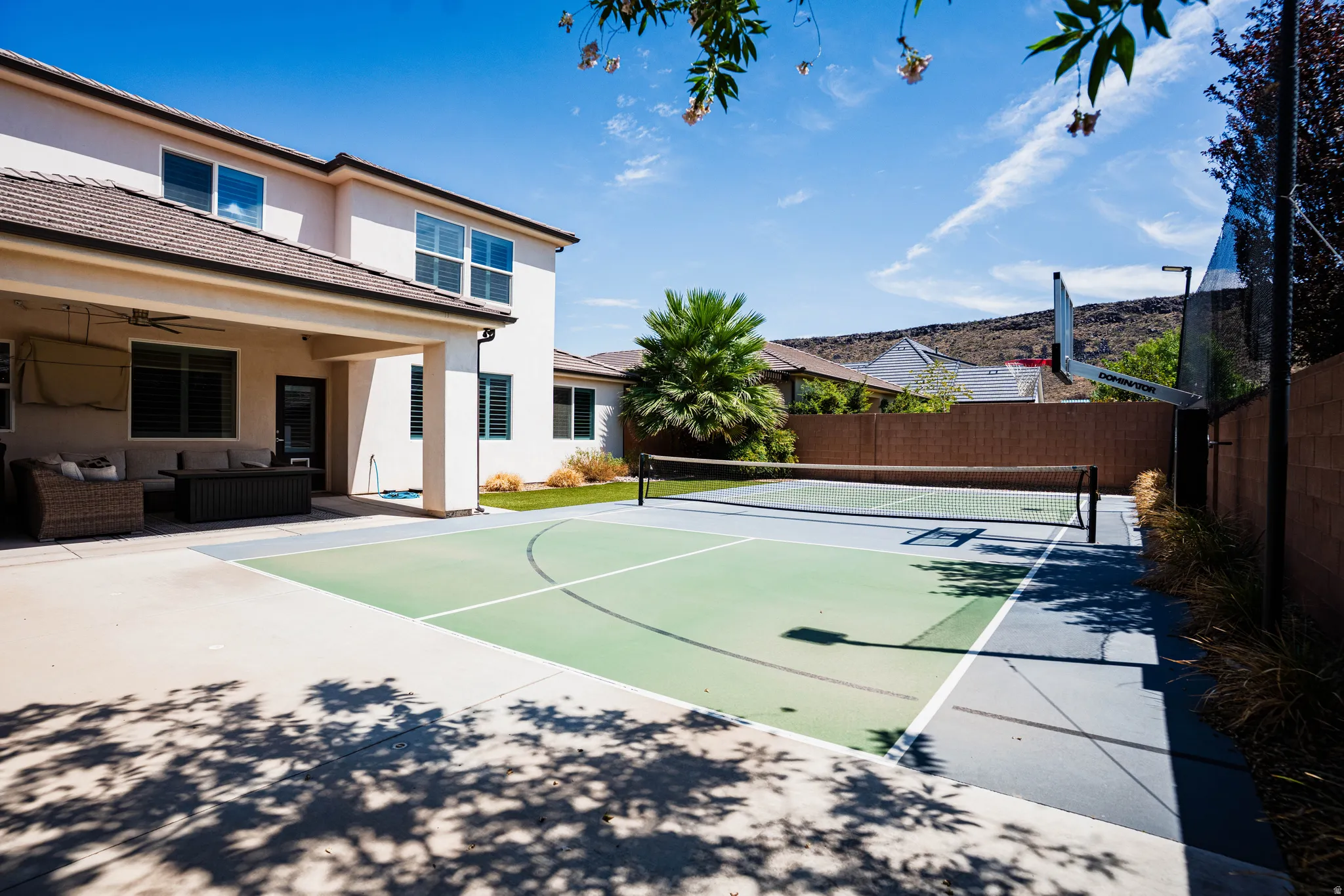 Sport court with integrated basketball hoop and net, alongside a covered patio with recessed lighting