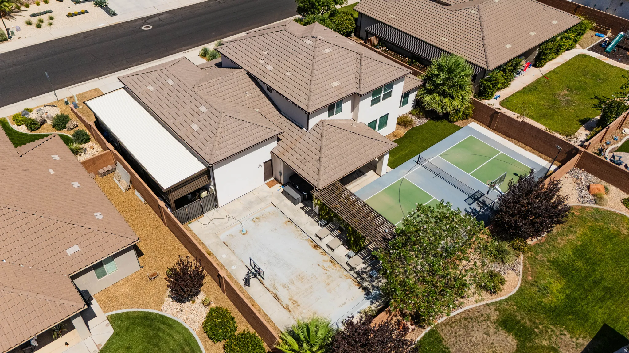 Tile roof, concrete patio, built-in sports court, perimeter fencing, and mature landscaping