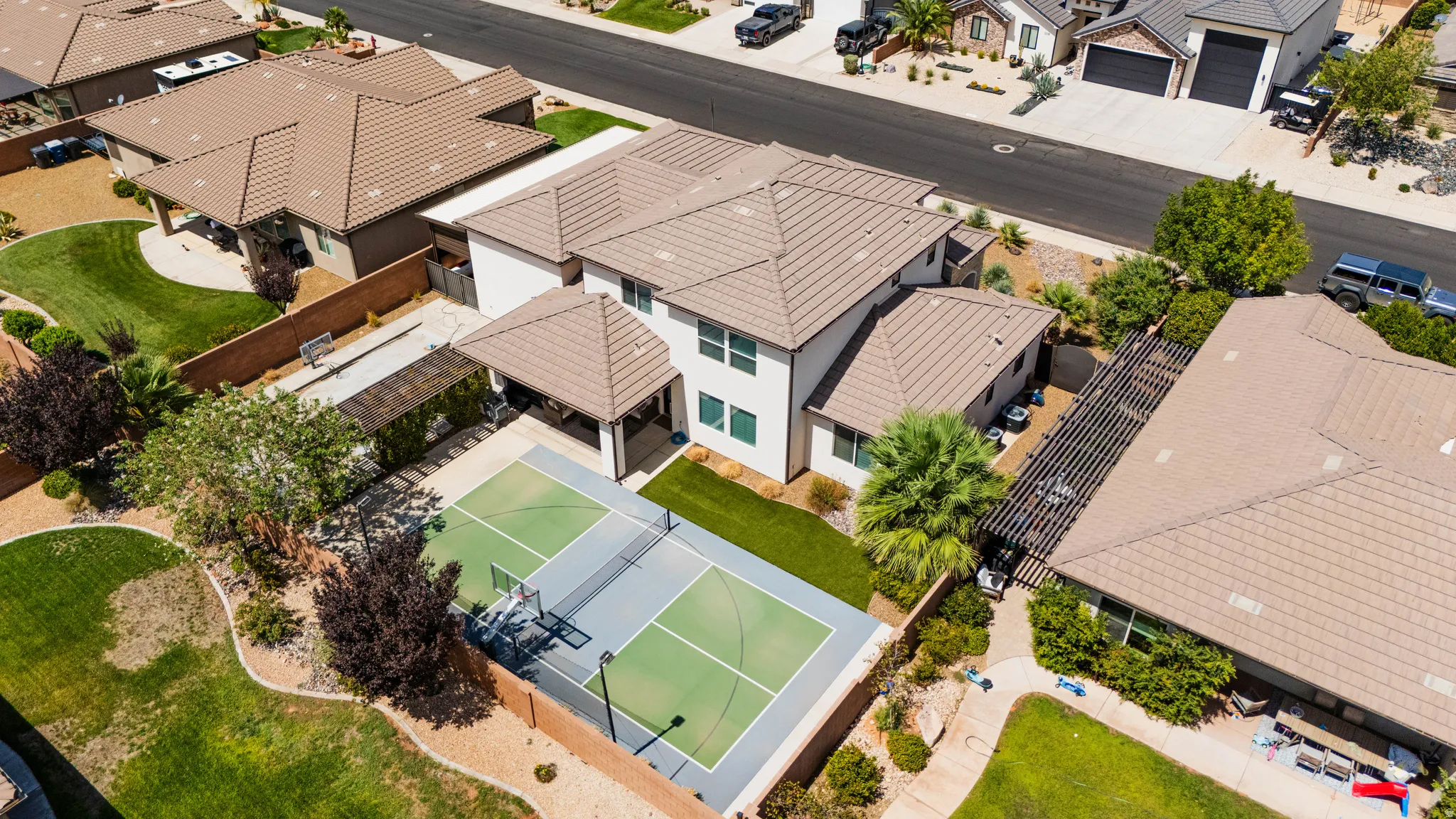 Full-size sport court, expansive backyard with manicured lawn, mature trees, covered patio, and tile roof