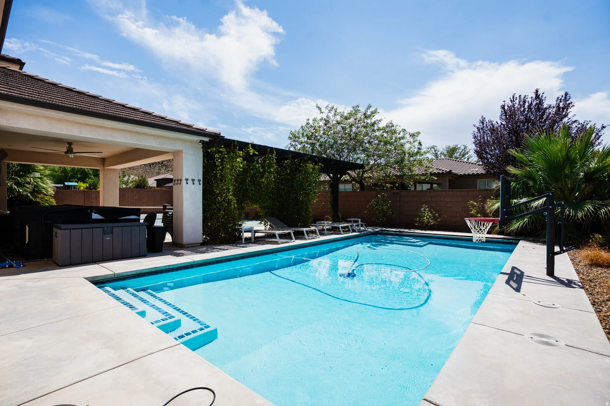 Outdoor swimming pool with integrated steps, concrete hardscaping, and an attached covered patio featuring a ceiling fan