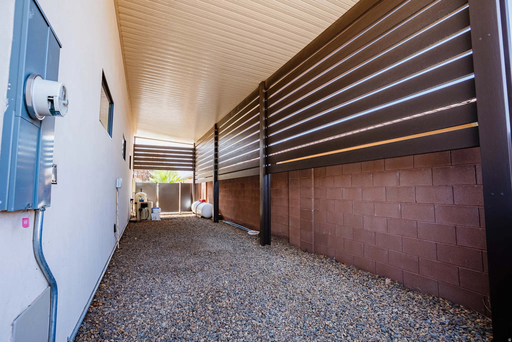 Covered side yard with gravel ground cover, brown block wall, and slatted fencing