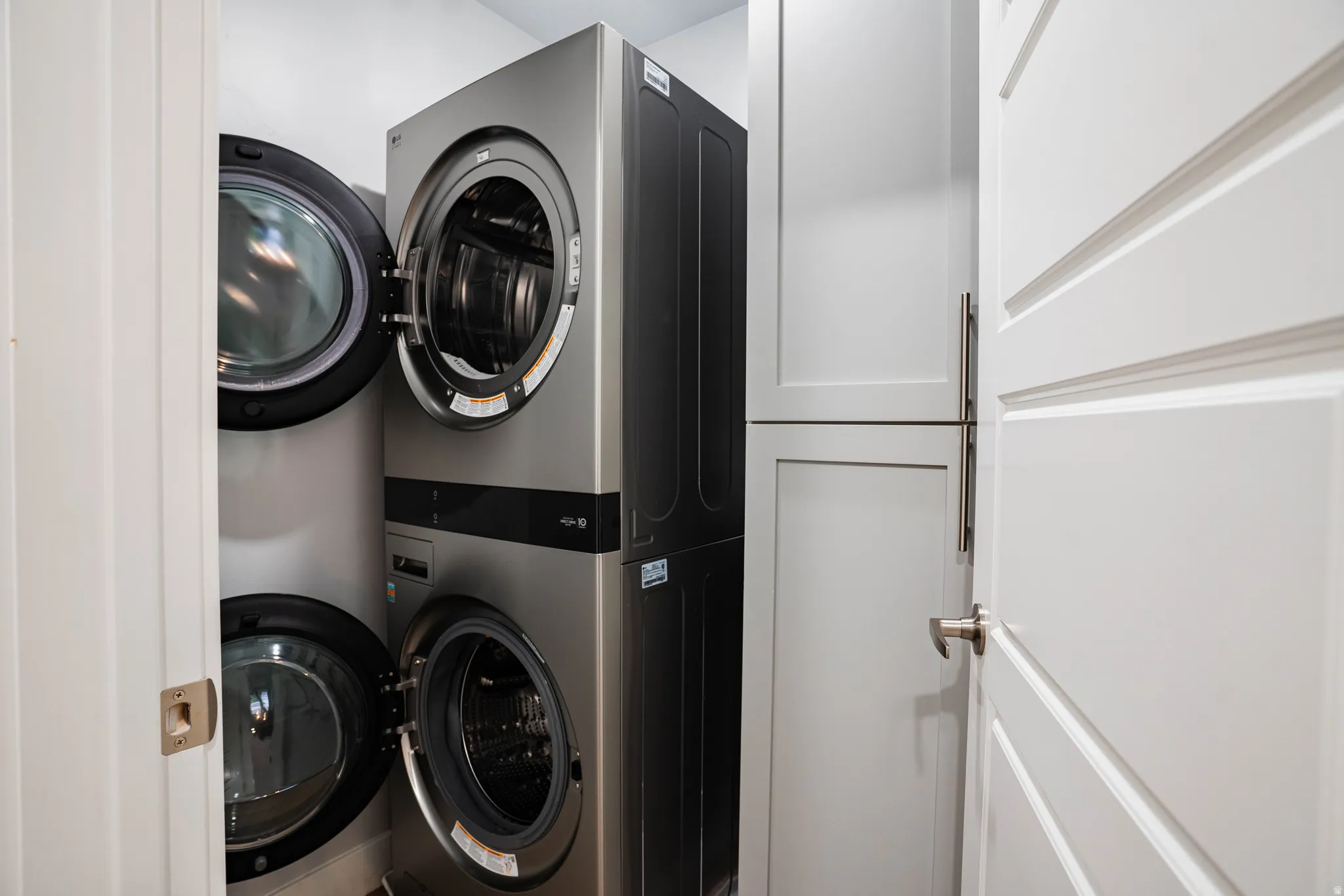 Stacked washer and dryer units with a white paneled door and light-toned cabinetry featuring brushed nickel pulls