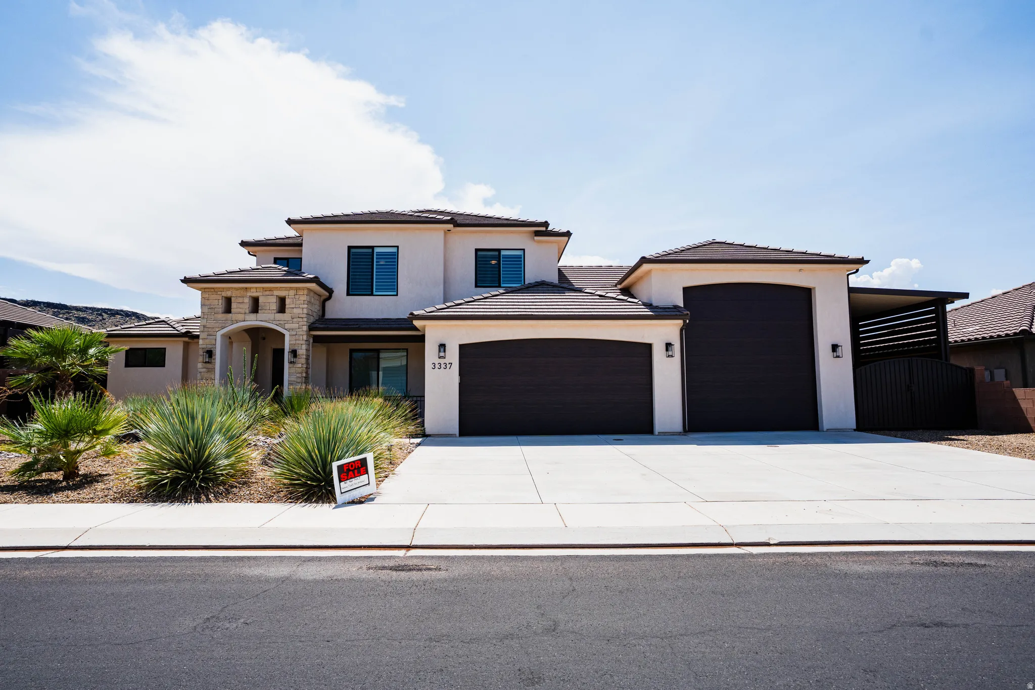 Stucco exterior with stone accents, dark garage doors, concrete driveway, and low-maintenance desert landscaping