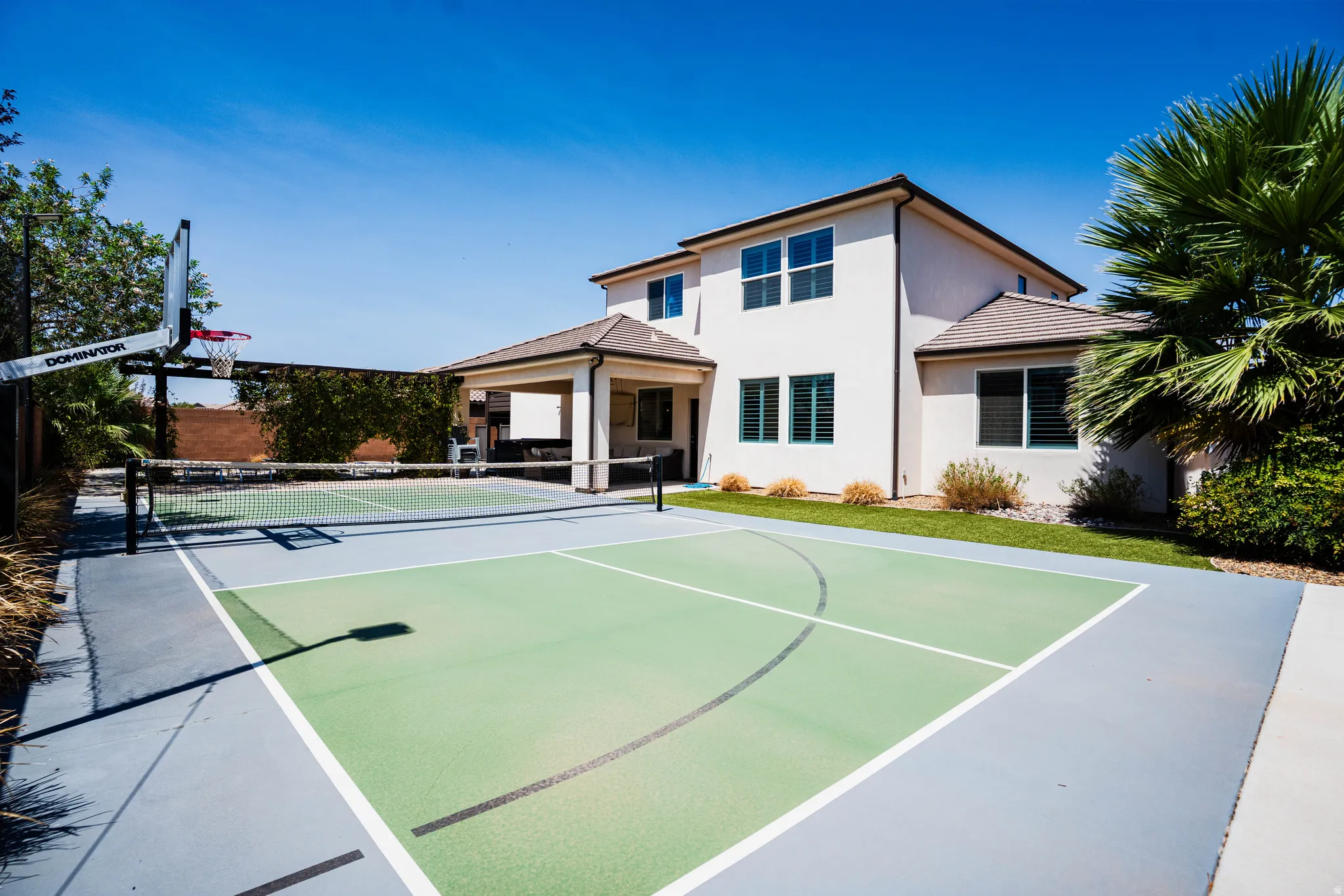 Multi-sport court with basketball hoop and net, covered patio, manicured lawn, and mature landscaping