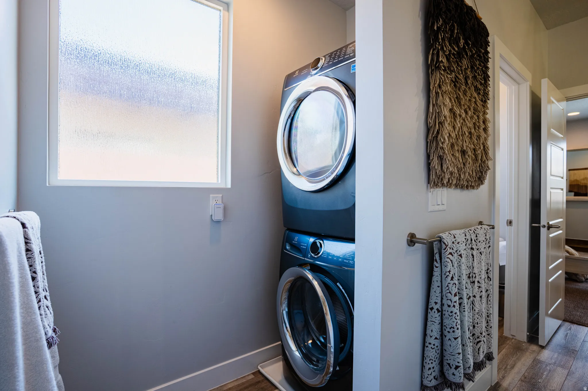 Stacked washer and dryer units, wood-finish flooring, and a frosted window