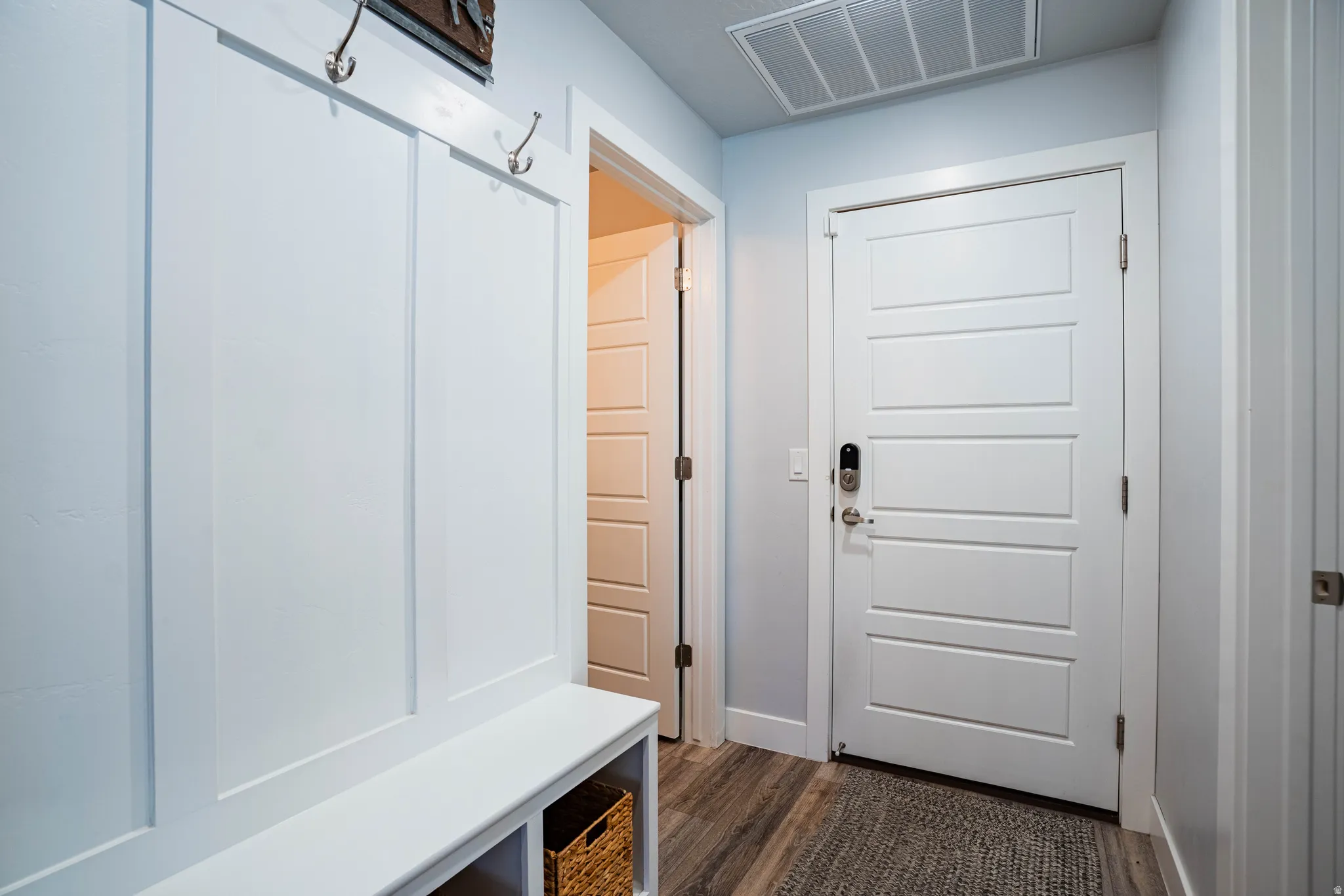 Built-in board and batten bench with storage, brushed nickel coat hooks, wood-finish flooring, and a paneled entry door