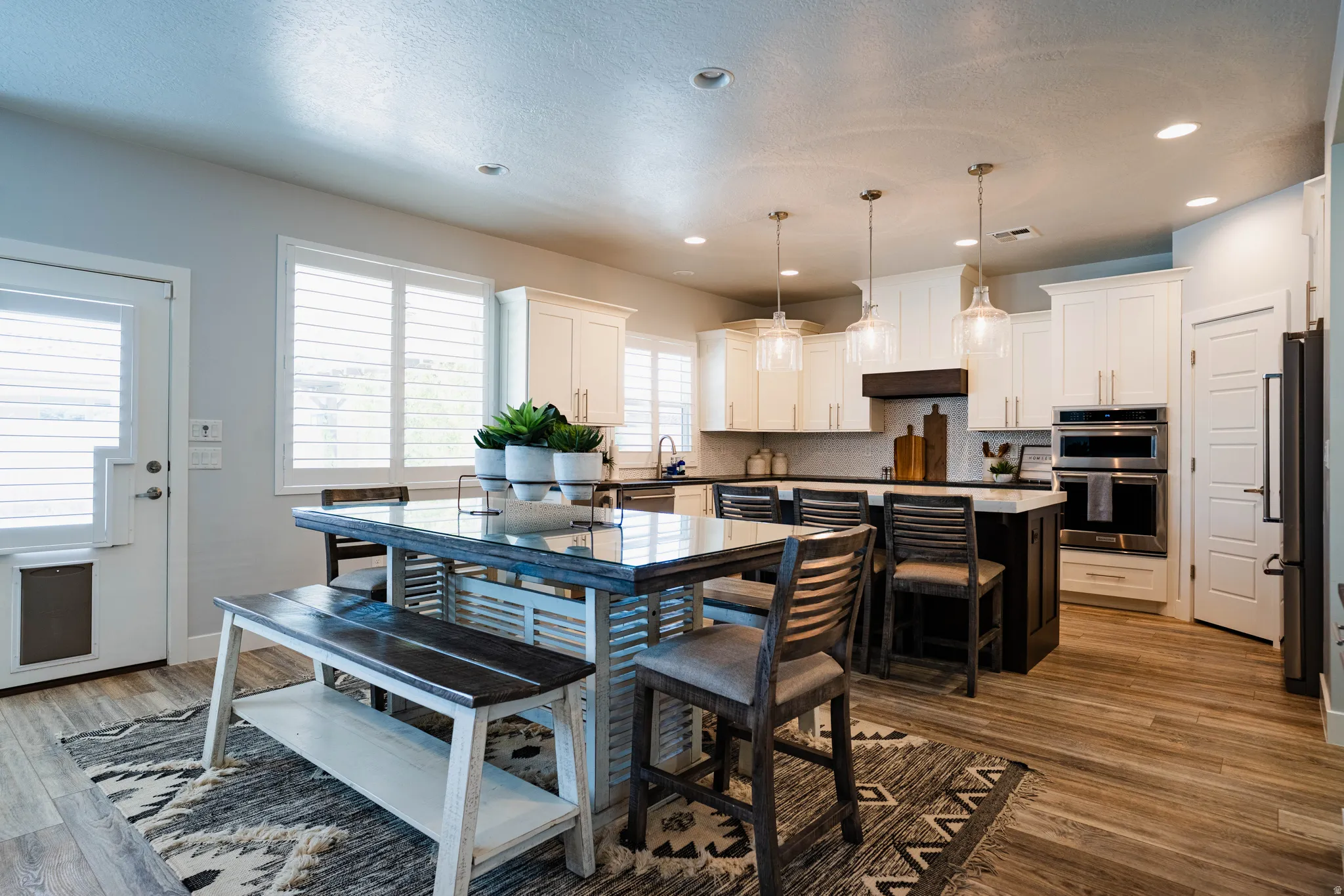 Modern kitchen featuring white shaker cabinetry, stainless steel appliances, an oversized island with seating, pendant lighting, and wood-finish flooring