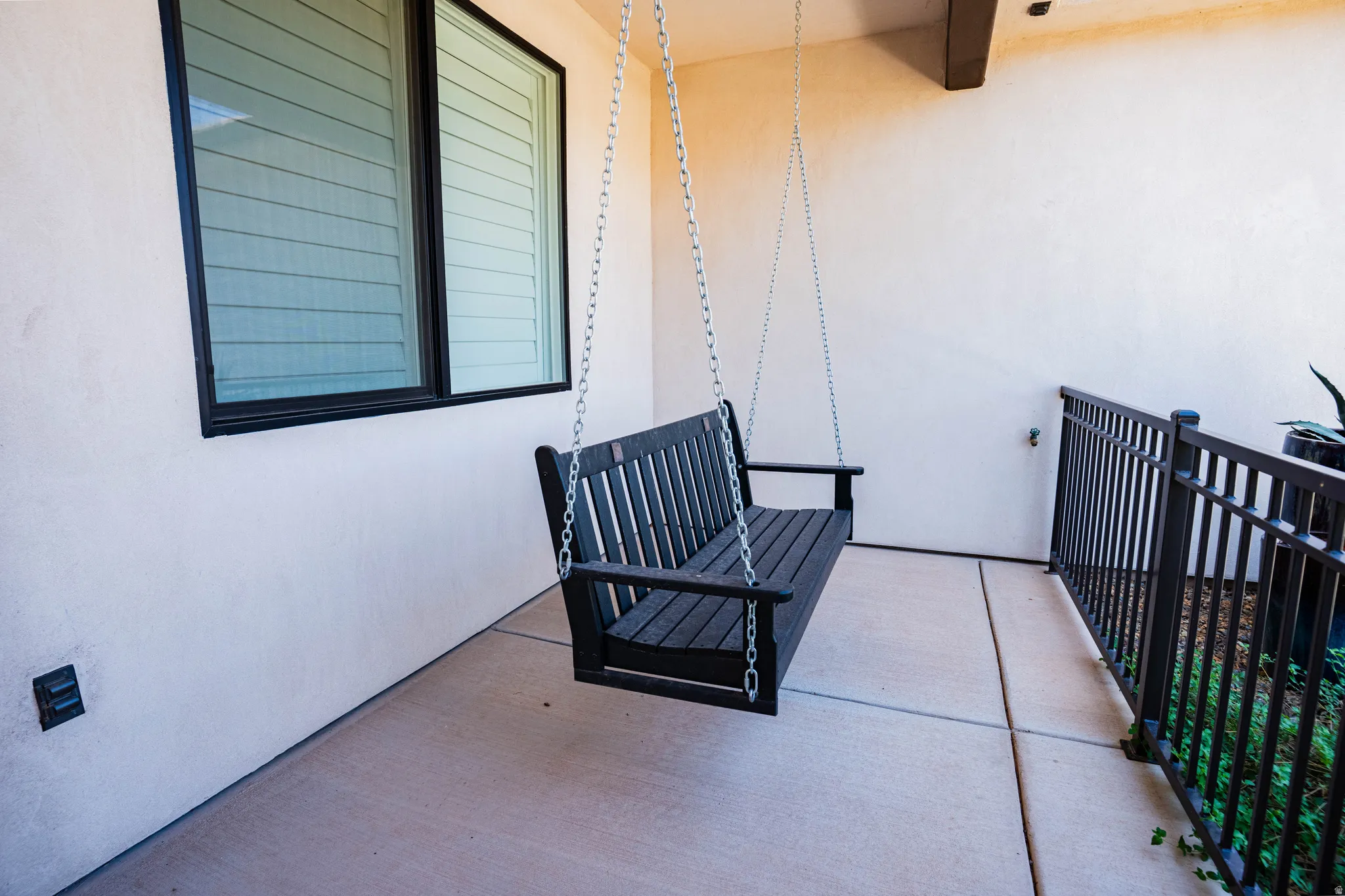 Patio featuring a concrete surface, a black metal railing, and a window with louvered blinds