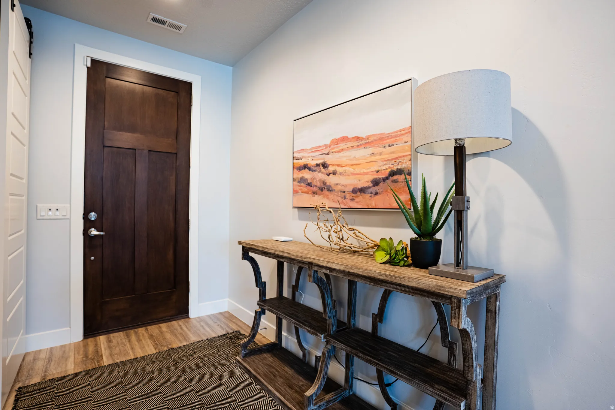 Rich wood door with panel detailing, wood-finish flooring, and a decorative console table with shelving