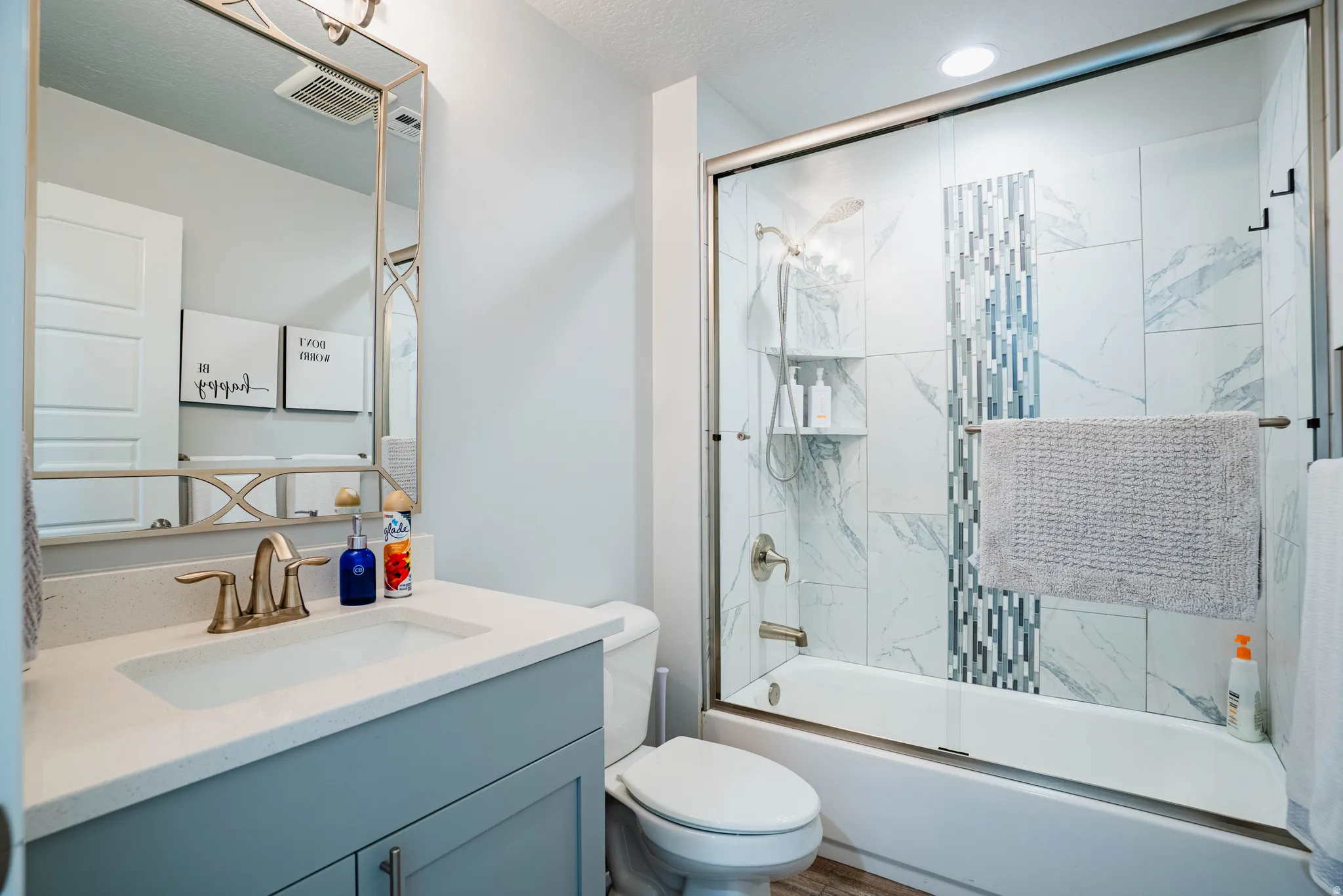 Bathroom featuring a modern vanity with integrated sink, a framed mirror, and a full bathtub with a glass enclosure