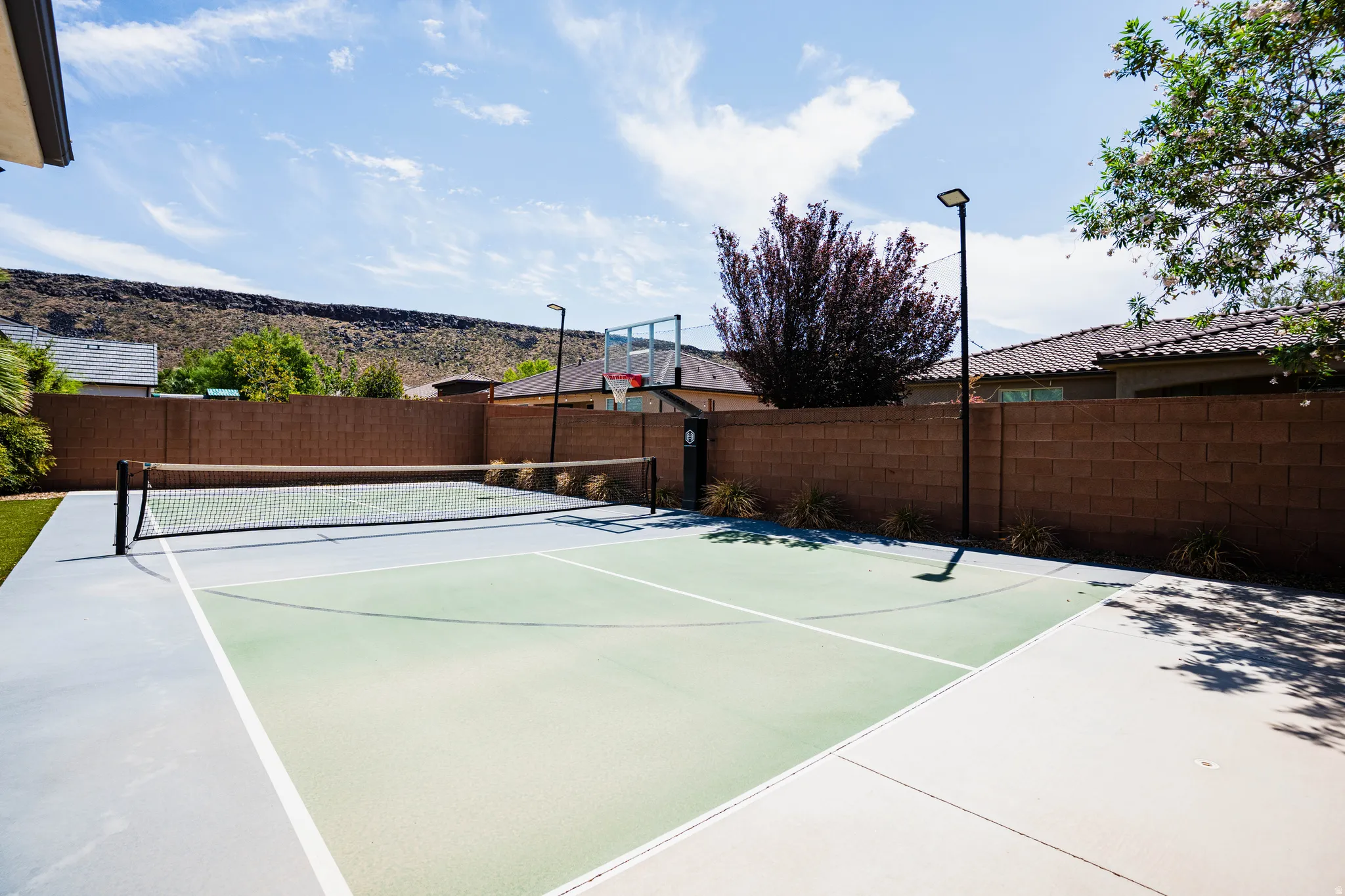 Multi-sport court with a net and integrated basketball hoop, bordered by a brick privacy wall