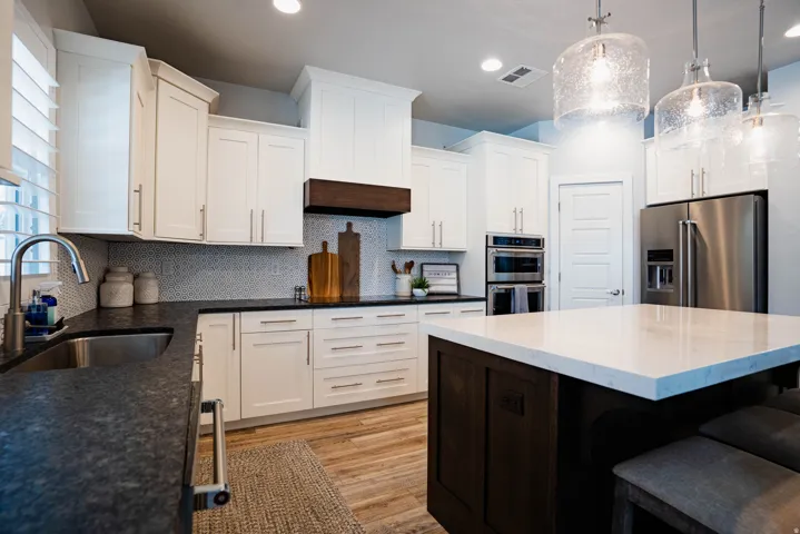 Gourmet kitchen featuring white cabinetry, dark stone countertops, stainless steel appliances, a center island with light-colored countertop, and wood-finish flooring