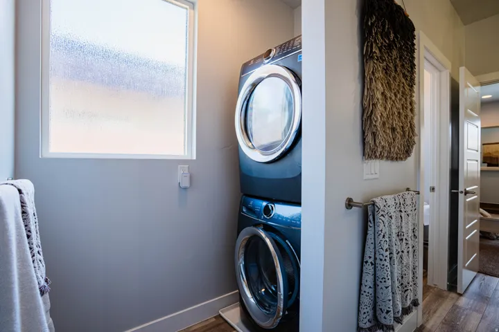 Stacked washer and dryer units, wood-finish flooring, and a frosted window