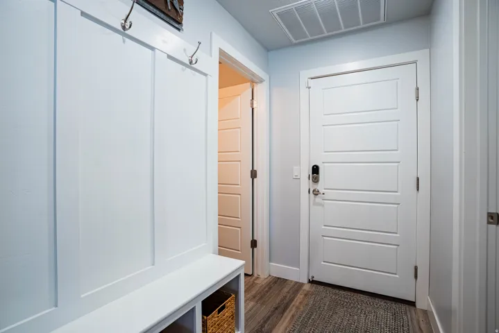 Built-in board and batten bench with storage, brushed nickel coat hooks, wood-finish flooring, and a paneled entry door