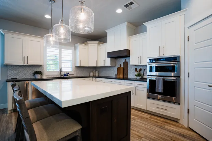 Kitchen featuring white shaker cabinetry, stainless steel double ovens, a large center island with seating, a dark wood-finish hood, and wood-finish flooring