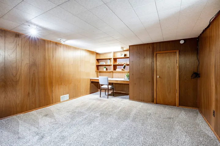 Recessed ceiling lighting, wood-paneled walls, built-in shelving, built-in desk, and light-colored carpet
