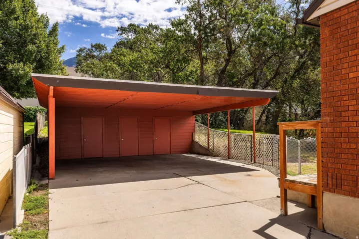 Carport with an orange ceiling and four storage doors, concrete driveway, and red brick exterior