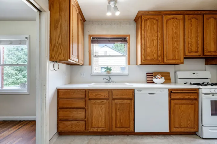 Wood-finish cabinetry with white countertops, integrated sink, and a built-in dishwasher