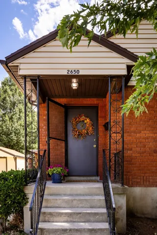 Brick exterior featuring a covered entry, concrete steps, wrought iron railing, and a dark-toned door
