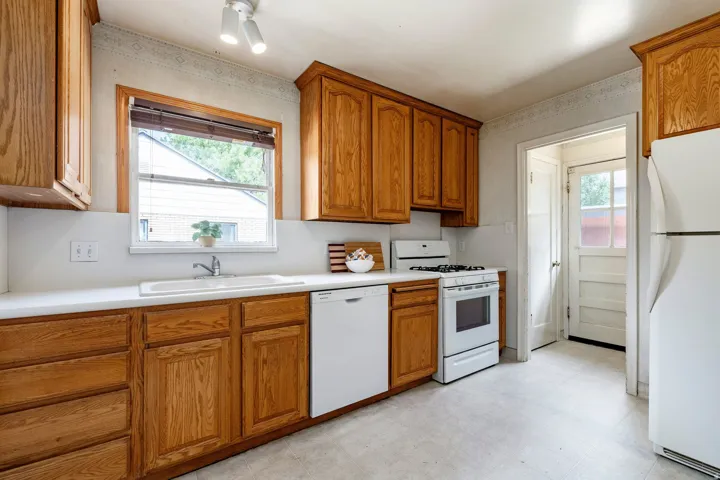 Wood cabinetry, white countertops, built-in dishwasher, and a window above the sink