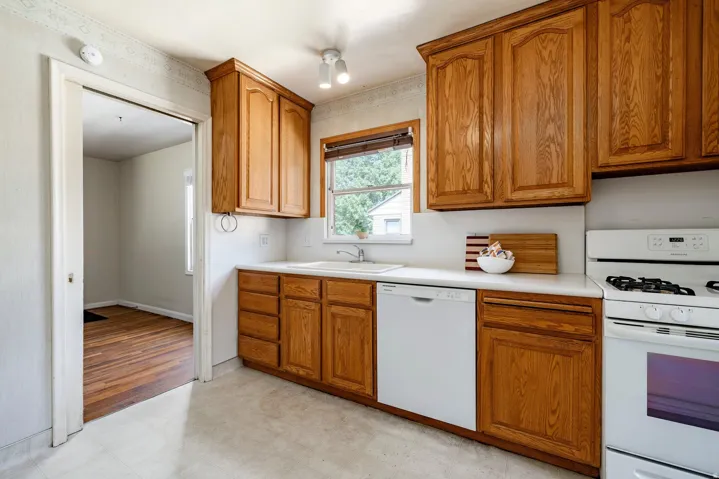 Wood-finish cabinetry, solid surface countertops, white tile-look flooring, and a white oven/range