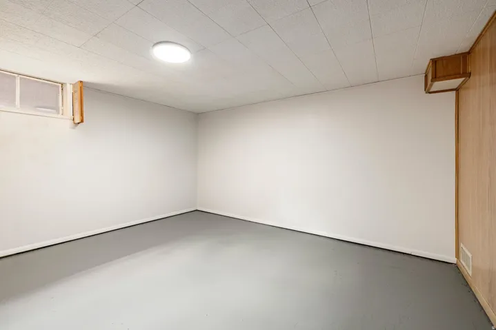 White painted walls, wood-paneled accent wall, concrete flooring, drop ceiling, and recessed lighting