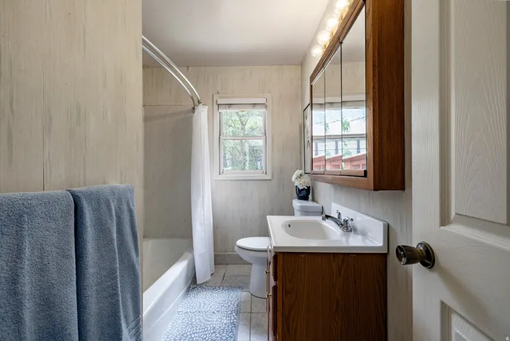 White bathroom vanity with a single basin sink, wall-mounted mirrored medicine cabinet, and overhead light fixture