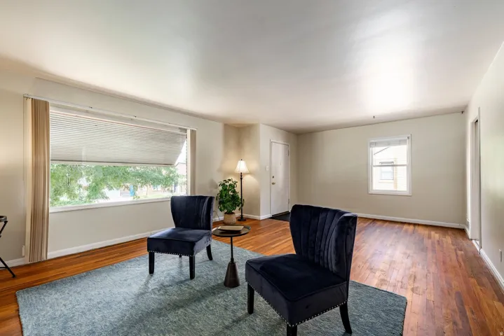 Hardwood flooring, painted walls, large window with blinds, additional window, and a white entry door