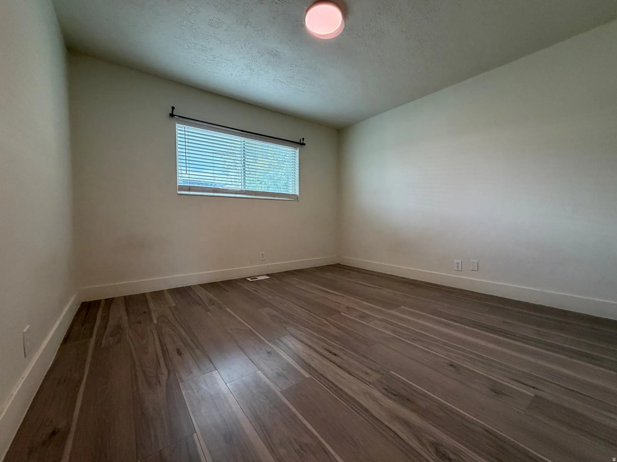 Wood-finish plank flooring, white wall paint, window with blinds, and flush-mount ceiling light