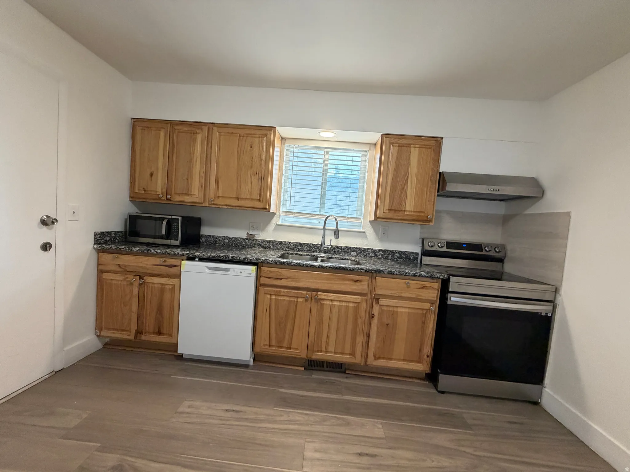 Kitchen featuring wood-finish cabinetry, speckled countertops, stainless steel appliances, and wood-look flooring