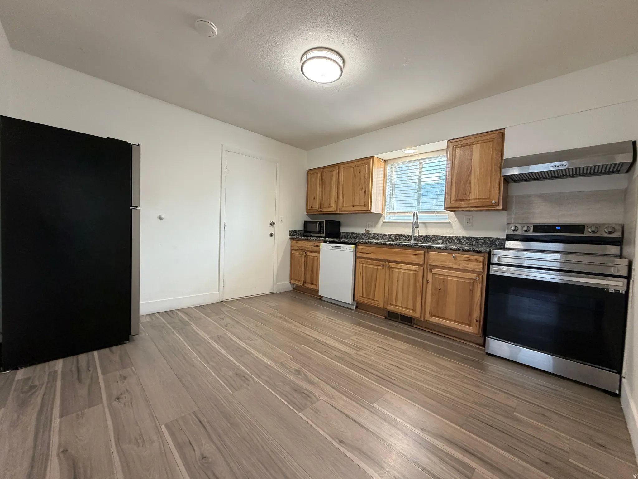 Wood-finish flooring, wood cabinetry, stone countertops, stainless steel range, and stainless steel range hood