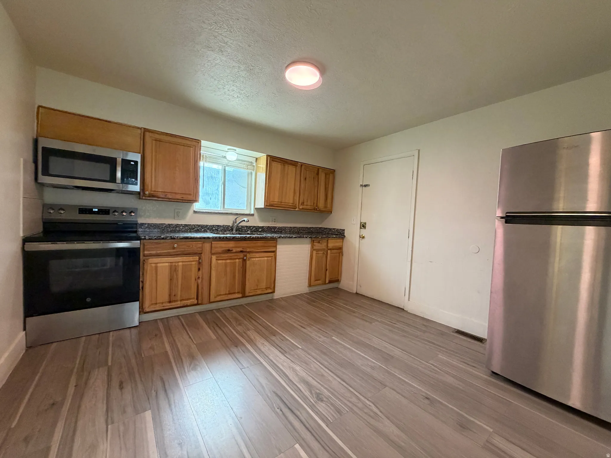 Wood-finish flooring with wood cabinetry, stainless steel appliances, and a built-in microwave