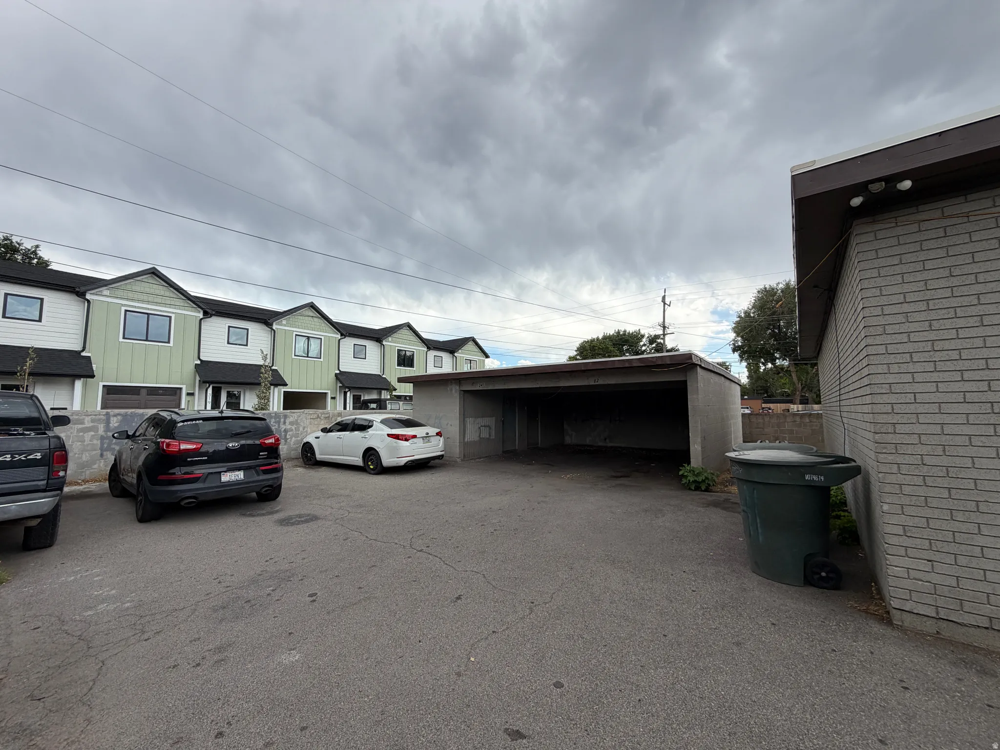 Paved lot featuring a covered parking structure, brick exterior, and multi-unit residential buildings