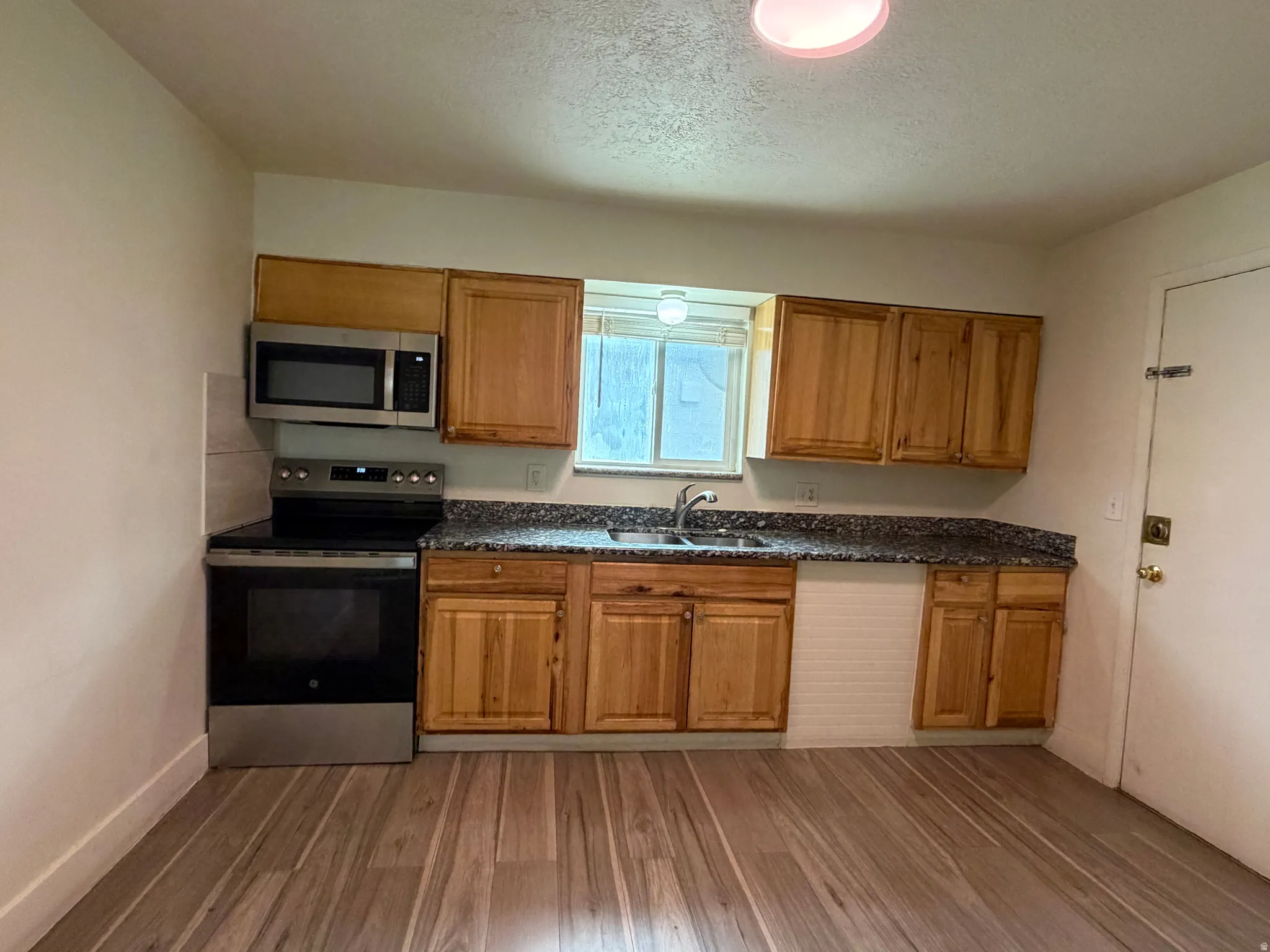 Kitchen featuring wood-finish cabinetry, dark speckled countertops, stainless steel appliances, and wood-finish flooring