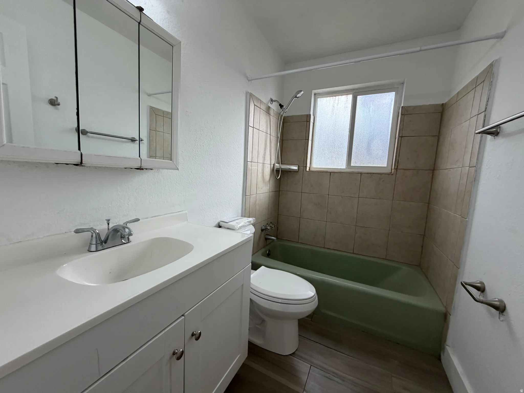 Full bathroom with vanity sink, medicine cabinet with mirrored doors, toilet, and bathtub/shower combination with tile surround and window for natural light