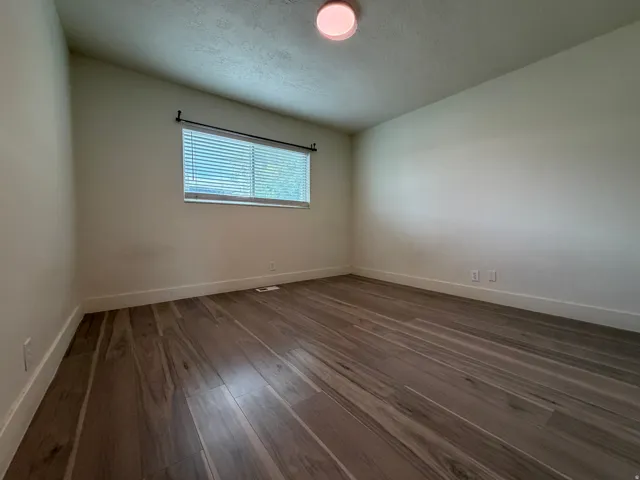Wood-finish plank flooring, white wall paint, window with blinds, and flush-mount ceiling light
