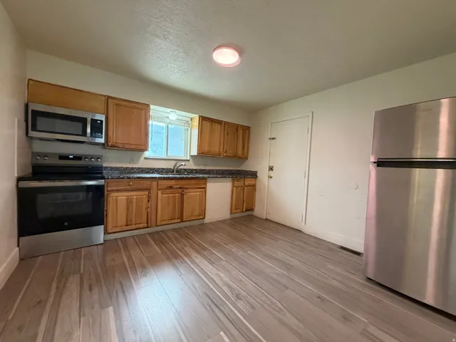 Wood-finish flooring with wood cabinetry, stainless steel appliances, and a built-in microwave
