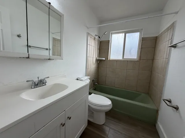 Full bathroom with vanity sink, medicine cabinet with mirrored doors, toilet, and bathtub/shower combination with tile surround and window for natural light
