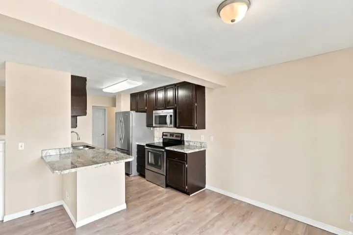 Kitchen featuring dark wood-finish cabinetry, stainless steel appliances, light-toned countertops, a breakfast bar, and wood-finish flooring