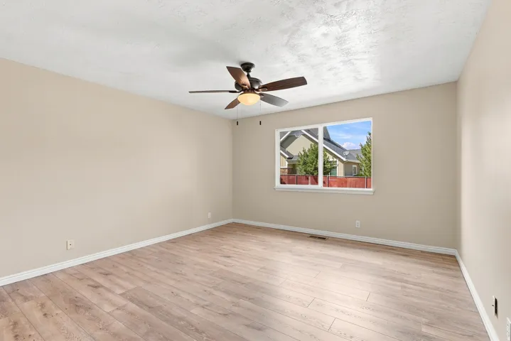 Spacious room featuring wood-finish flooring, a contemporary ceiling fan with integrated lighting, and neutral wall tones