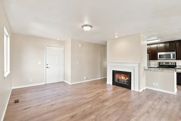 Wood-finish flooring, white trim, recessed lighting, fireplace with mantel, and dark wood kitchen cabinetry