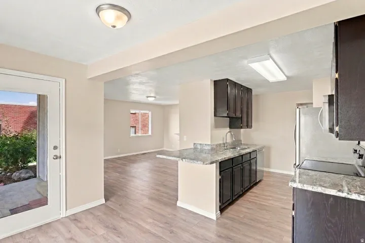 Kitchen featuring dark wood-finish cabinetry, light stone countertops, stainless steel appliances, and wood-finish flooring