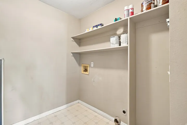 Wall-mounted shelving with laundry hookups and patterned tile flooring