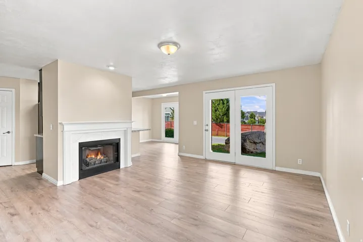 Living area featuring wood-finish flooring, a fireplace with a white mantel, and double glass doors