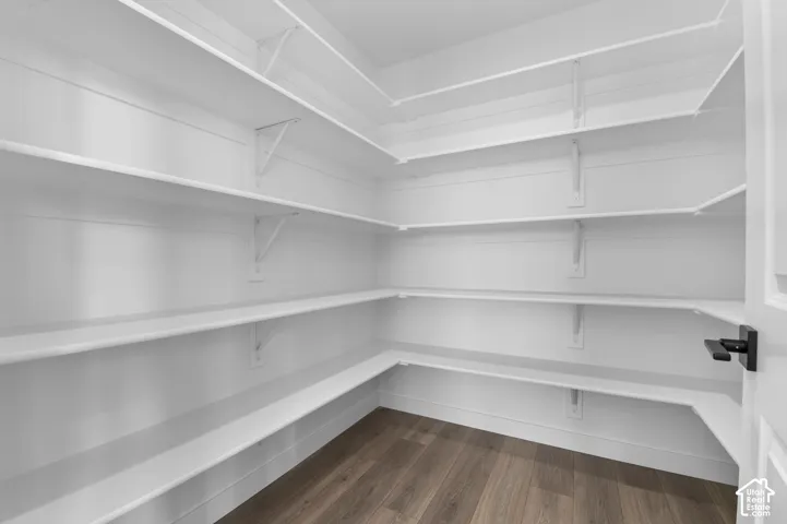 Expansive corner pantry featuring multiple levels of white shelving, wood-finish flooring, and a modern black door handle