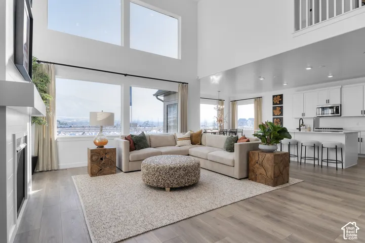 Two-story living area with high ceilings, wood-finish flooring, a white fireplace, and large windows