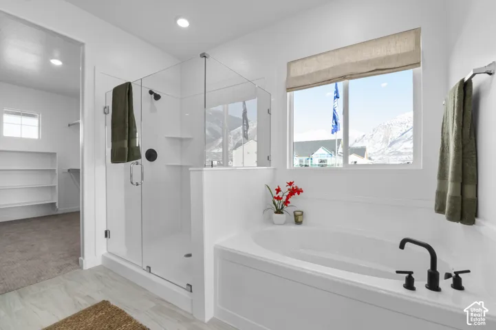 Soaking tub with matte black fixtures, glass-enclosed shower, wood-finish flooring, recessed lighting, and a window with a natural fiber shade