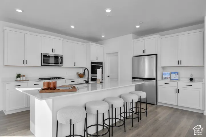 Spacious kitchen featuring white cabinetry, stainless steel appliances, a large center island with a sink, and wood-finish flooring